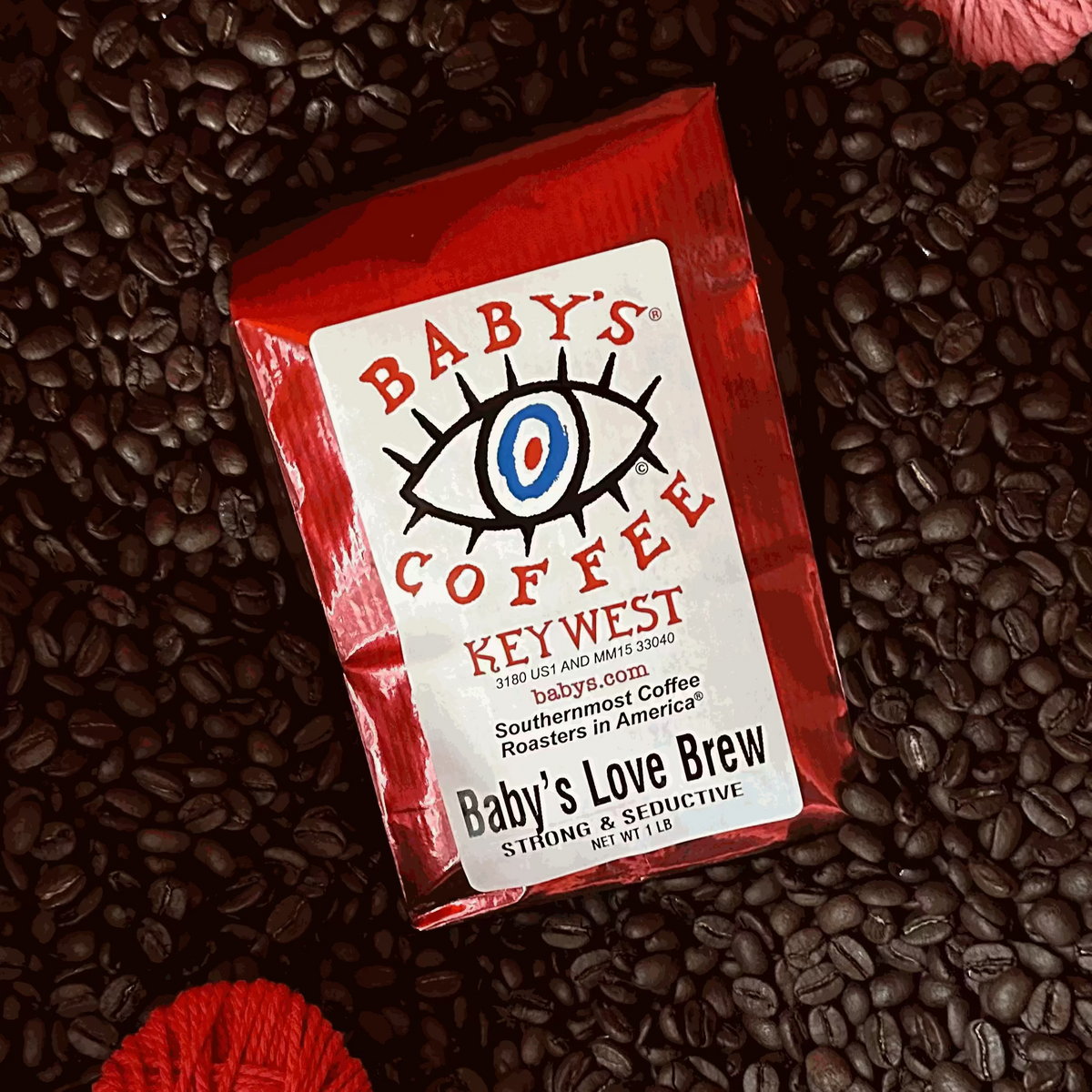 A red bag of Baby’s Love Brew coffee on roasted coffee beans