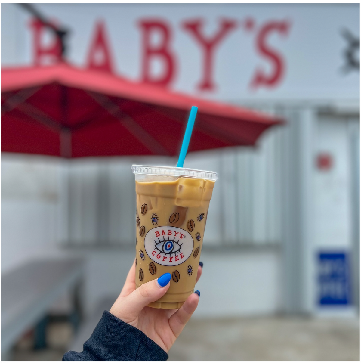 An iced coffee held outside the original Baby’s Coffee storefront