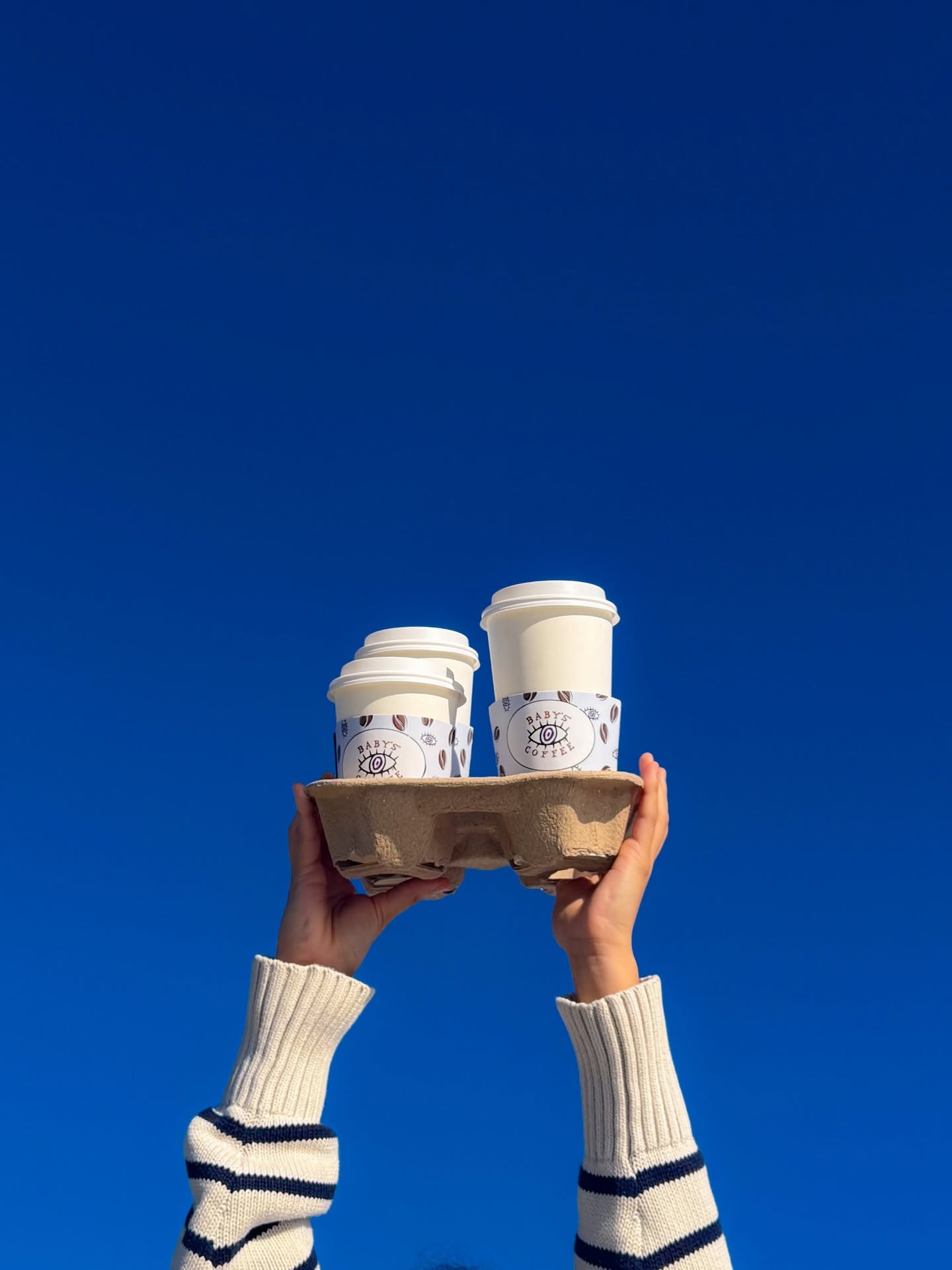 Baby’s Coffee takeaway cups held up against a clear blue sky